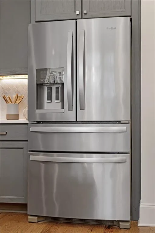 Room details featuring light hardwood / wood-style flooring, stainless steel fridge, decorative backsplash, and gray cabinetry