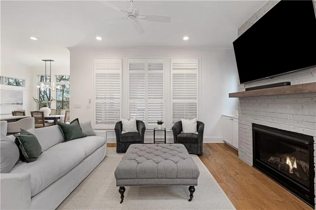 Living room with a brick fireplace, ceiling fan with notable chandelier, and light hardwood / wood-style flooring