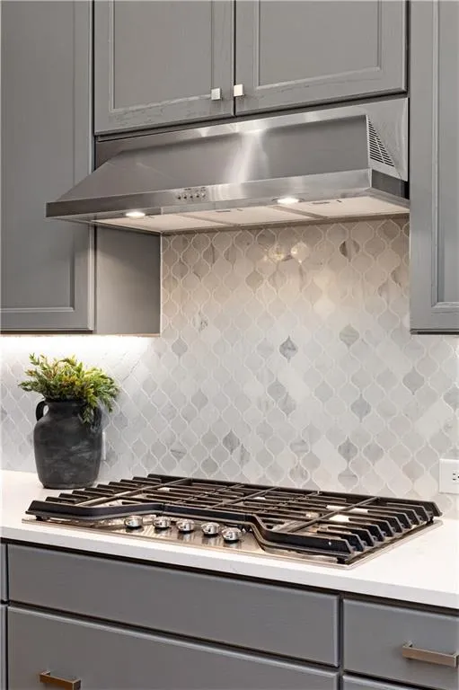 Kitchen with extractor fan, decorative backsplash, gray cabinets, and stainless steel gas stovetop