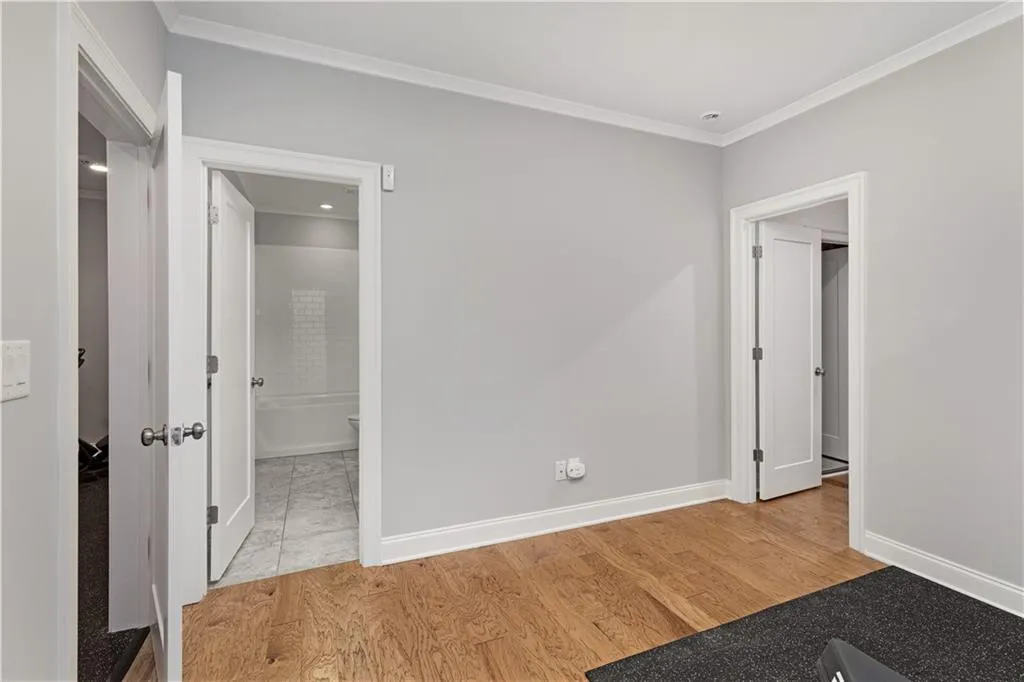 Unfurnished bedroom featuring crown molding, ensuite bath, and light wood-type flooring