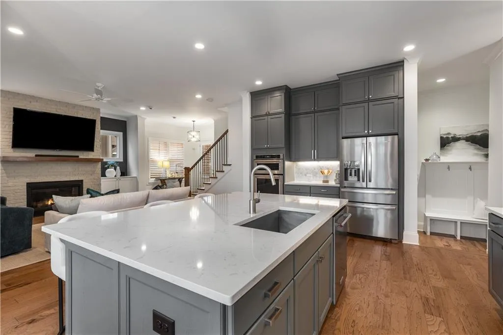 Kitchen featuring gray cabinets, appliances with stainless steel finishes, an island with sink, sink, and light stone countertops