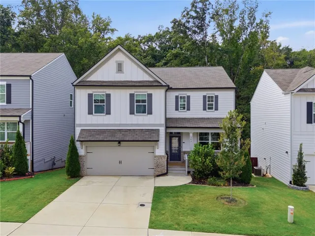 Two-story residence featuring light-colored siding with dark shutters, an attached two-car garage, covered entry, and a concrete driveway
