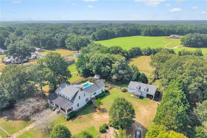 Expansive property featuring a main residence with a swimming pool, a secondary dwelling, and verdant surroundings including mature trees and open fields