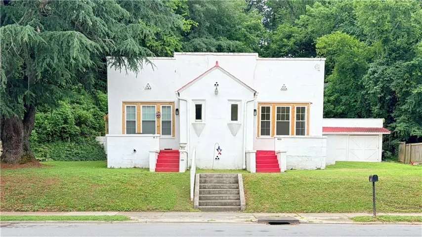 Classic cottage-style residence featuring a symmetrical white exterior with gabled roofline, golden-toned wood-frame windows, and red accent doors
