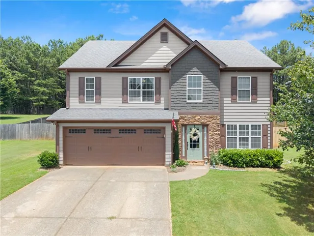 Two-story residence featuring a two-car garage, stone facade accents, decorative window shutters, a light blue entry door, and a manicured lawn