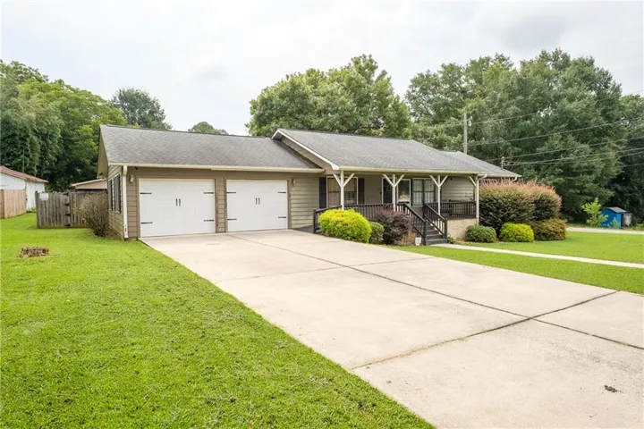 Single-story residence featuring a two-car garage with carriage-style doors, a covered front porch with dark railings, a concrete driveway, and established front landscaping