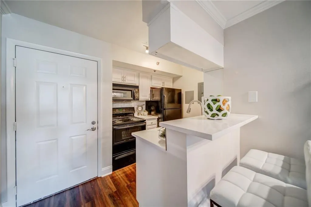 Kitchen with black appliances, crown molding, dark wood finished floors, a peninsula, and backsplash