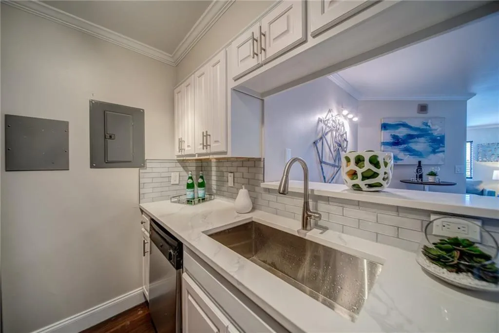 Kitchen featuring tasteful backsplash, ornamental molding, light stone countertops, white cabinetry, and electric panel