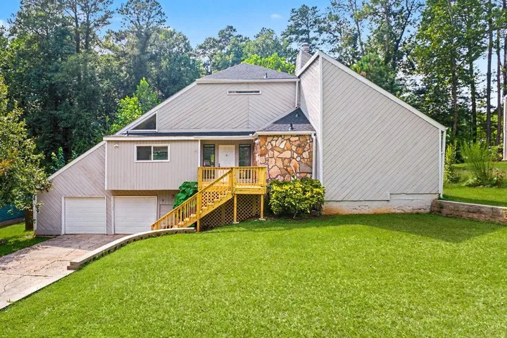 Contemporary exterior featuring a stone accent wall, multi-level design, wood-finish deck with stairs, two-car garage, and sloped front lawn