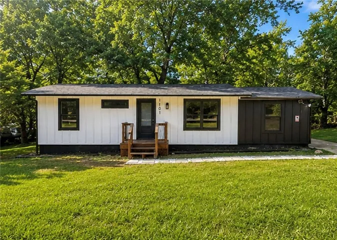 Single-story residence featuring white vertical siding, black trim accents, a dark entry door, and a contrasting dark horizontal siding section
