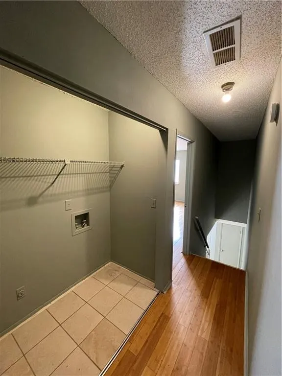 Laundry room with light wood-style floors, hookup for a washing machine, and a textured ceiling
