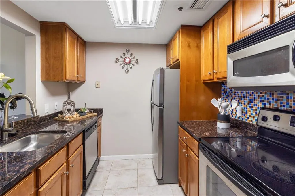 Kitchen featuring visible vents, brown cabinets, a sink, dark stone counters, and stainless steel appliances