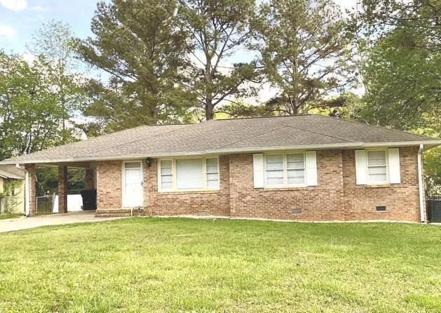 Brick ranch-style residence featuring a covered carport, white front door, and multiple windows with white shutters