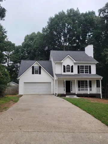 Two-story residence with white siding and dark shutters, featuring a covered front porch, an attached garage, and a concrete driveway