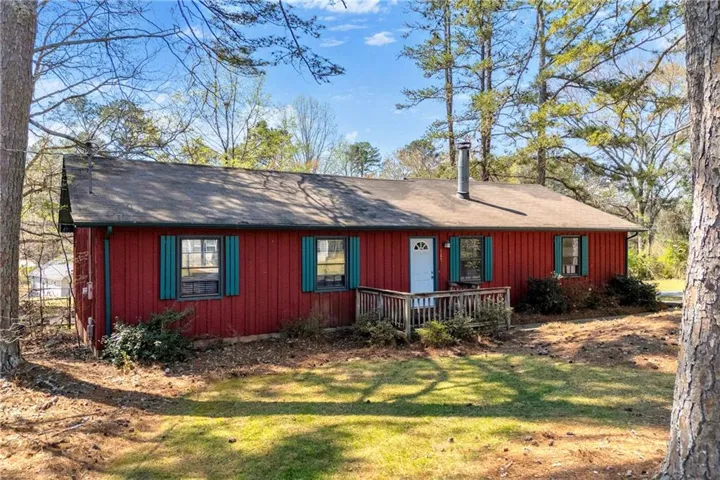 Single-story residence featuring red siding, a dark shingle roof, and teal shutters