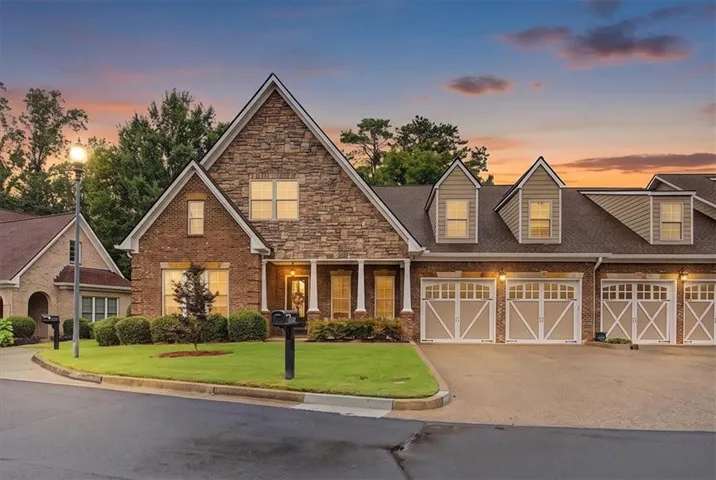 Brick and stone facade residence featuring a covered porch entry, dormer windows, and a manicured lawn