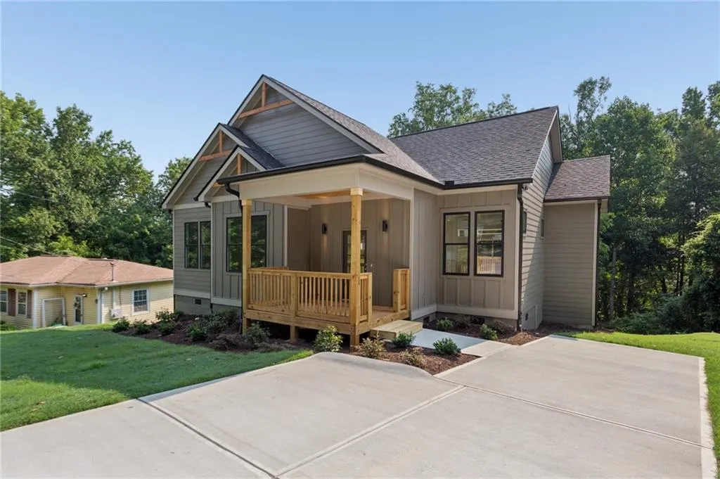 Contemporary home with light gray siding, dark asphalt shingles, a covered front porch with a wood railing, a concrete driveway, and a manicured lawn