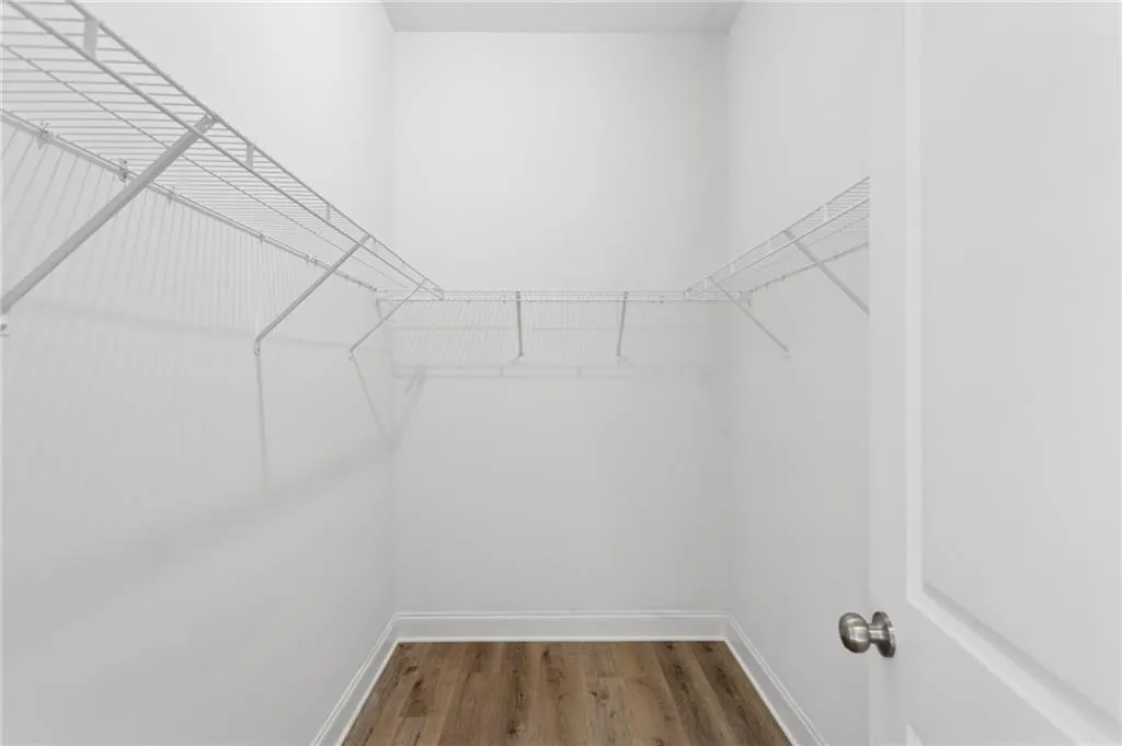 Walk-in closet featuring wire shelving, wood-finish flooring, white baseboards, and a white interior door with a brushed nickel knob