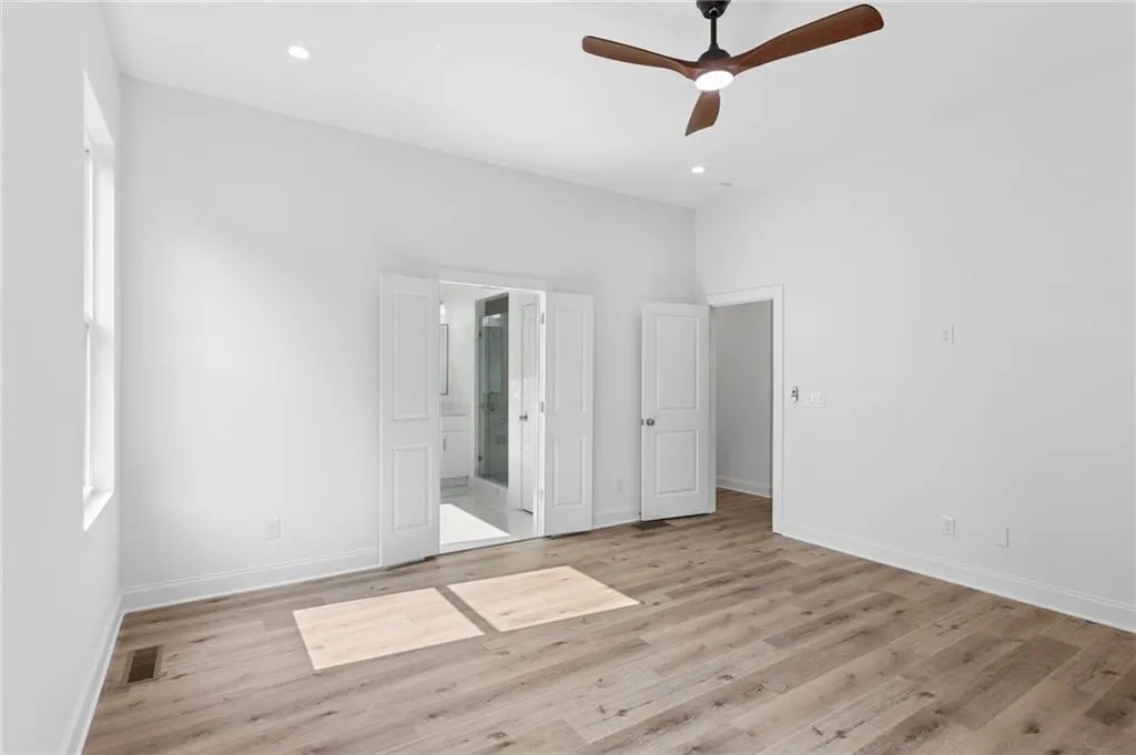 Spacious room featuring light wood-finish flooring, white walls, and a contemporary ceiling fan