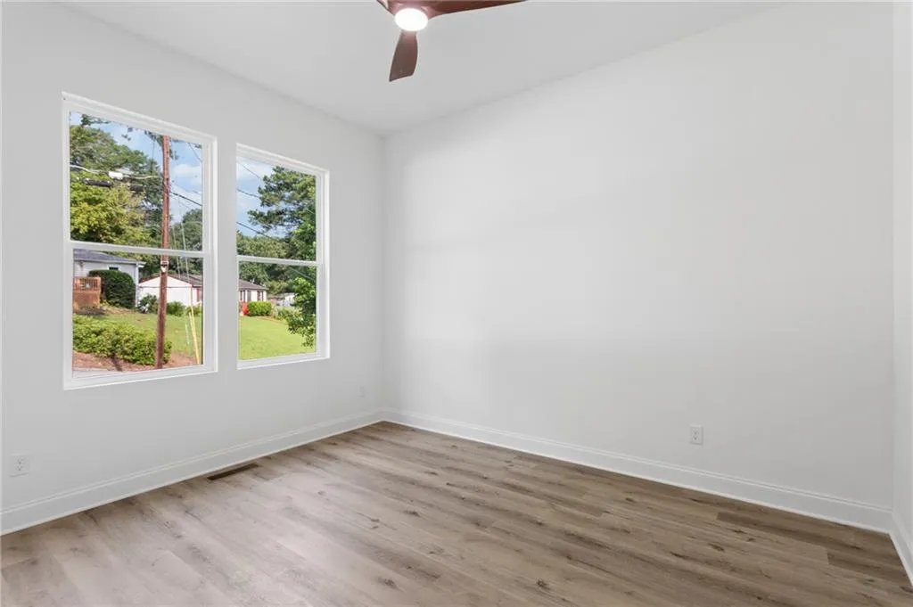 Bright room featuring two large windows, wood-finish flooring, white baseboards, a ceiling fan, and white walls