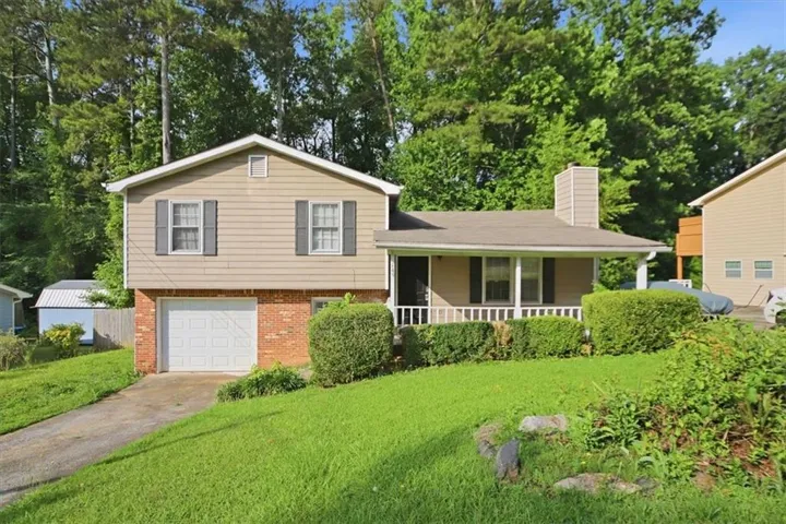 Split-level home featuring a front porch with white railings, a single-car garage, and a brick foundation