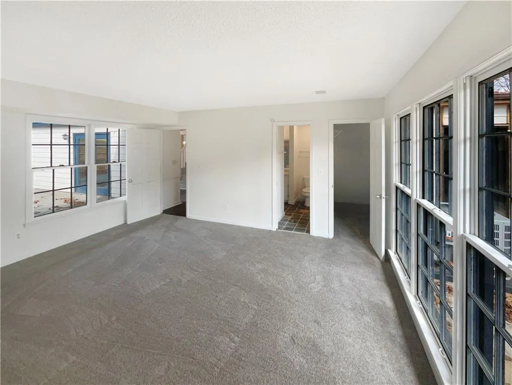 Unfurnished bedroom with multiple windows, a spacious closet, carpet, connected bathroom, and a textured ceiling