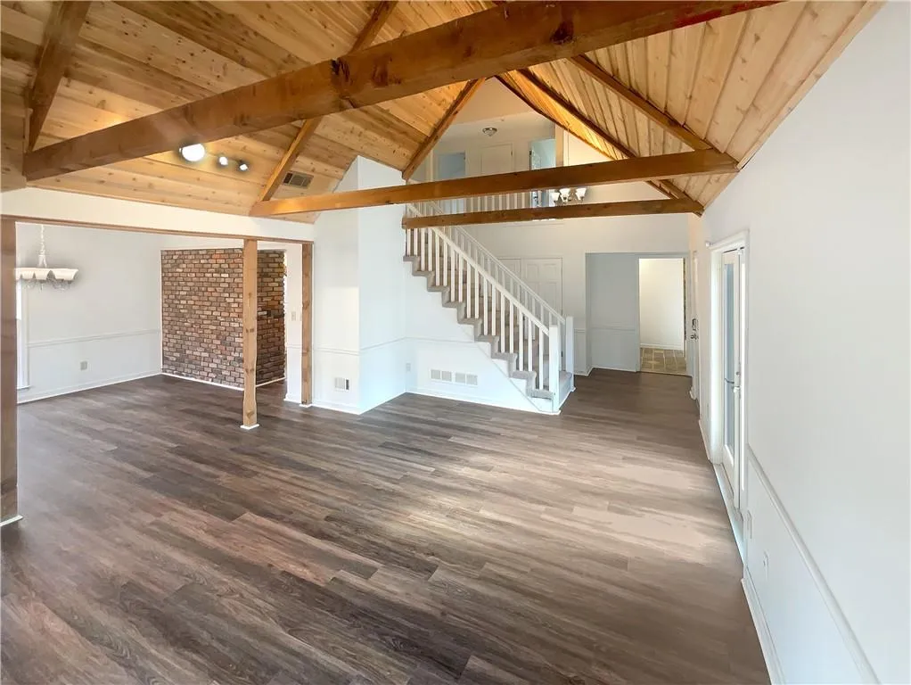Unfurnished living room featuring stairway, dark wood-type flooring, a wooden ceiling with exposed beams, and high vaulted ceiling