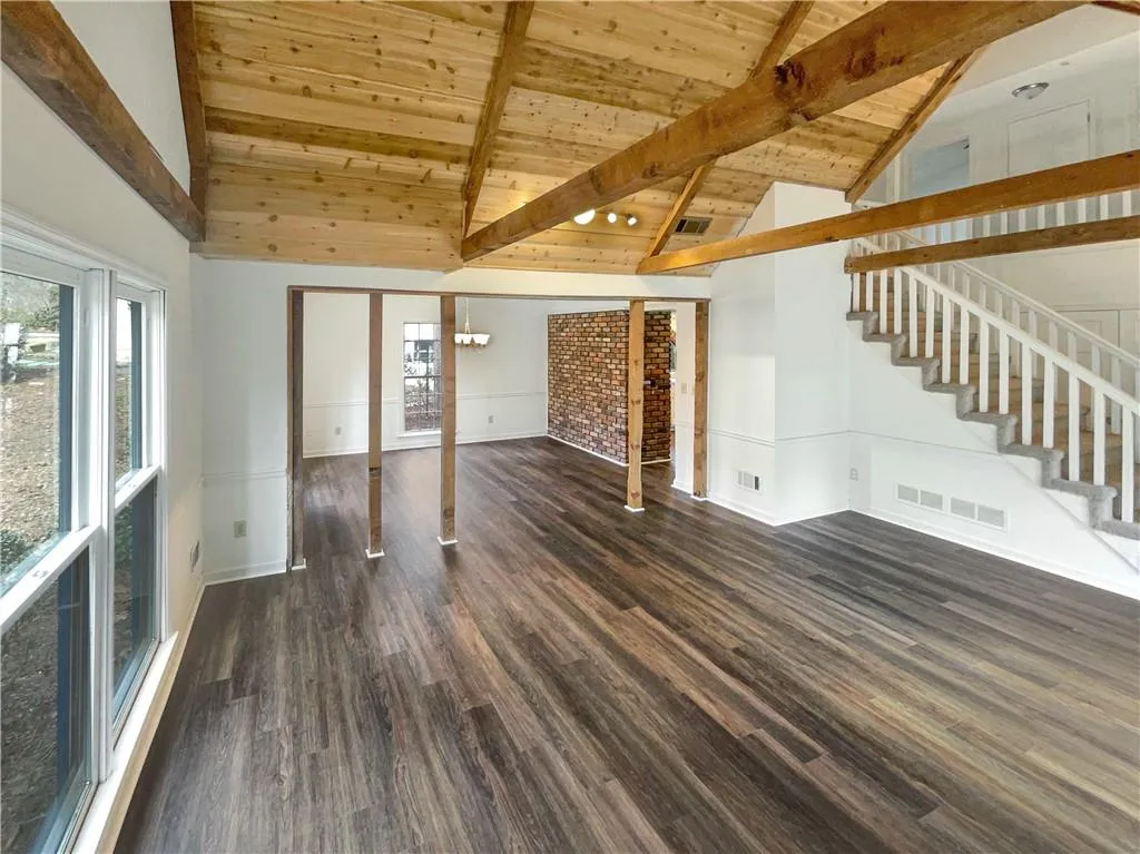 Unfurnished living room with stairs, dark wood-type flooring, a wooden ceiling with exposed beams, and high vaulted ceiling
