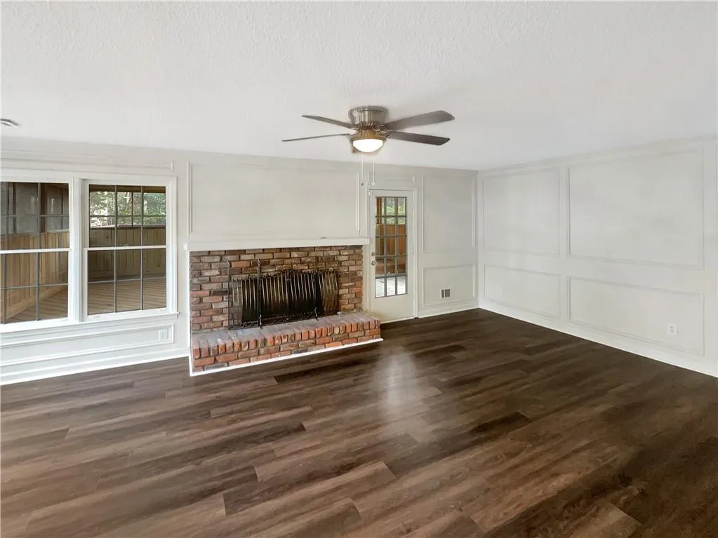 Unfurnished living room featuring a decorative wall, dark wood-style floors, a fireplace, plenty of natural light, and a textured ceiling