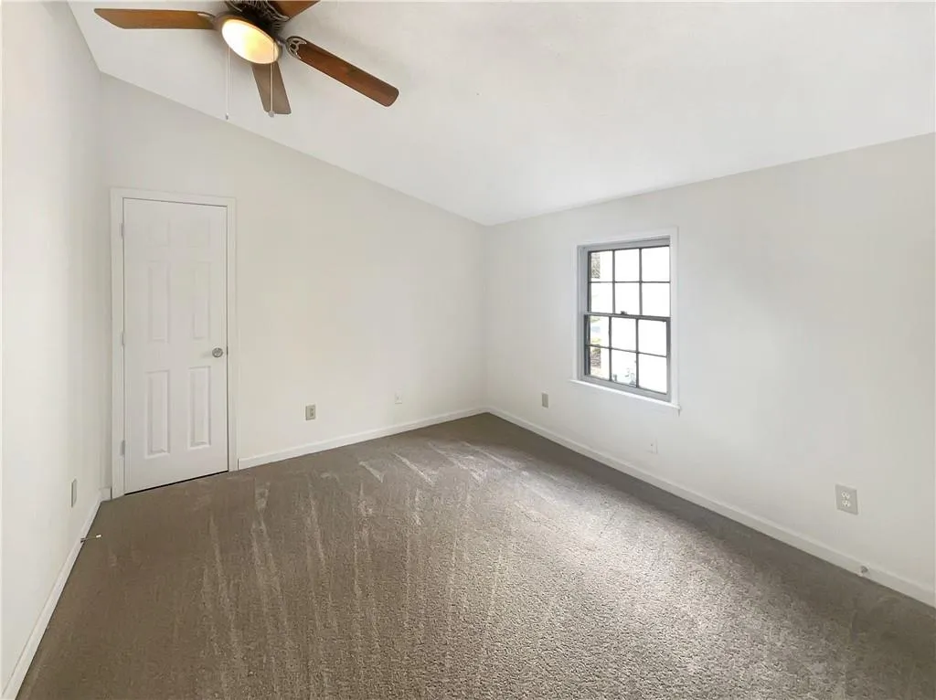 Empty room featuring vaulted ceiling, dark colored carpet, and a ceiling fan