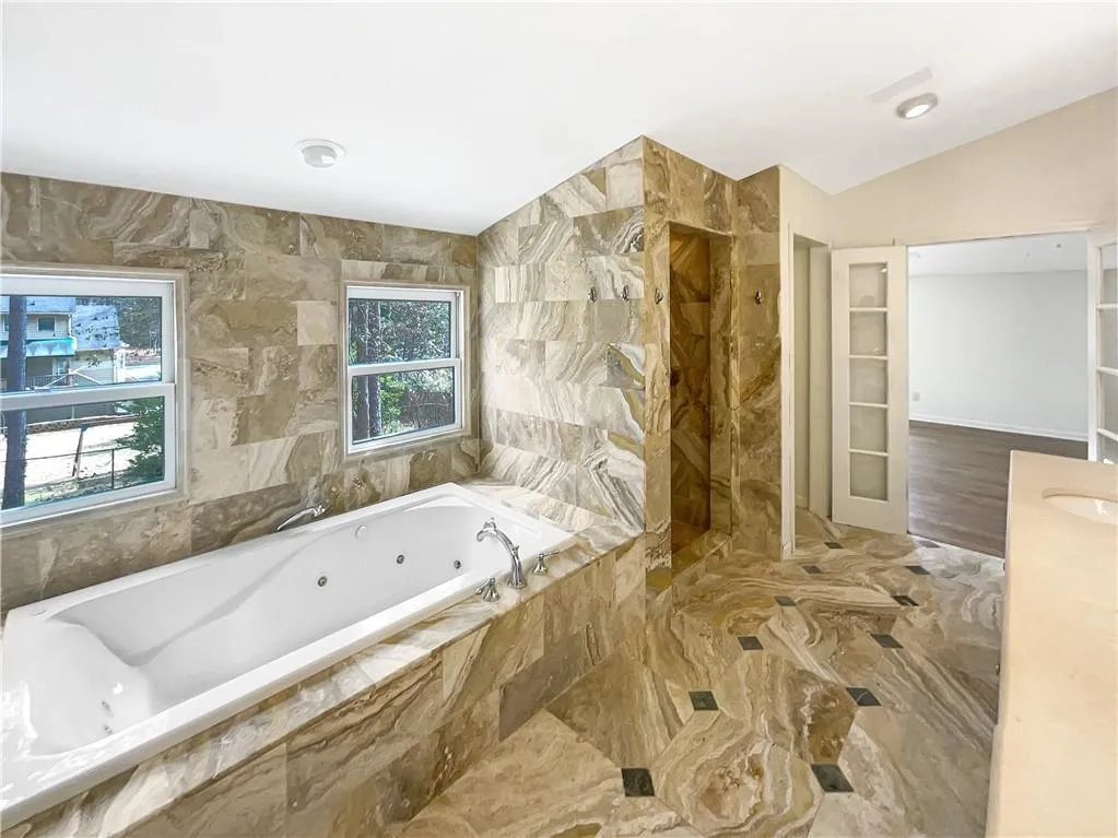 Full bathroom featuring a jetted tub, vanity, a marble finish shower, vaulted ceiling, and tile walls