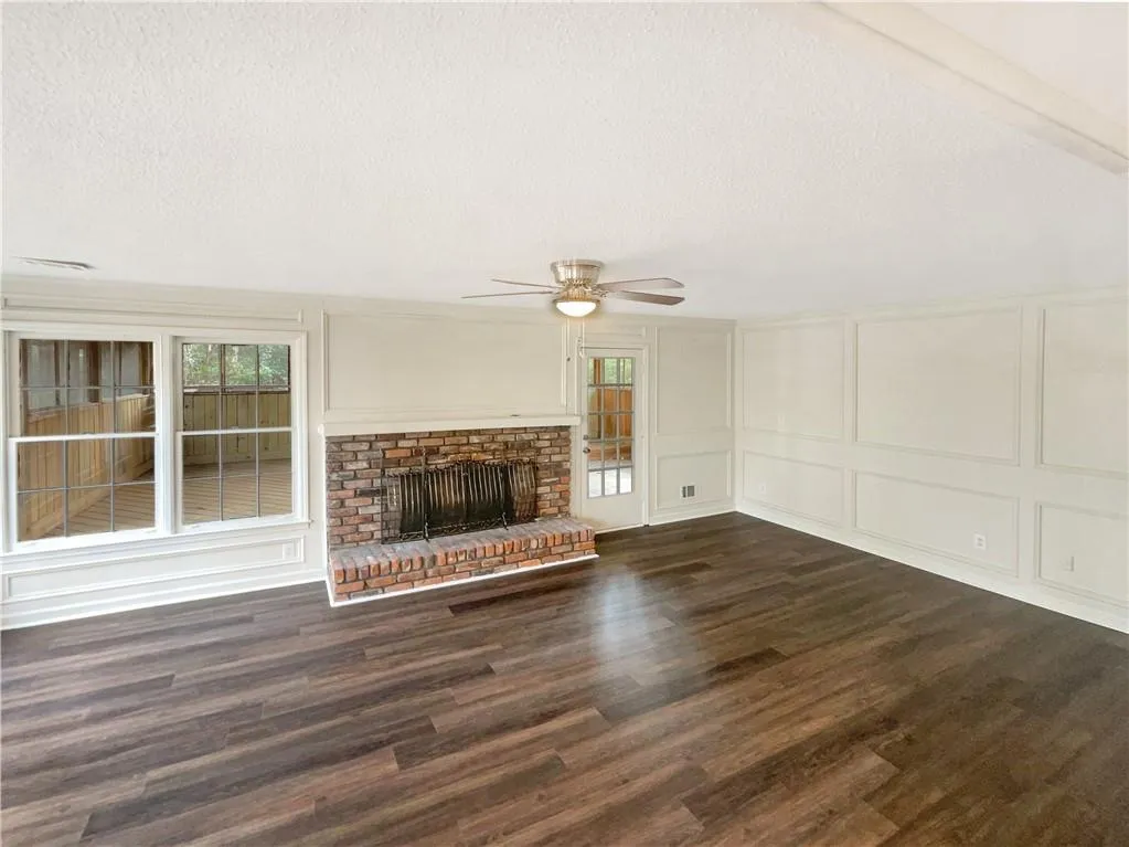 Unfurnished living room with a decorative wall, a textured ceiling, dark wood-style flooring, a fireplace, and healthy amount of natural light