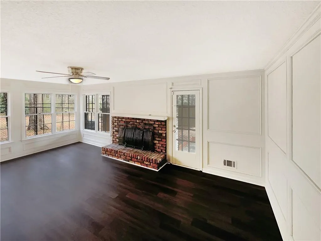Unfurnished living room featuring a decorative wall, a fireplace, ceiling fan, dark wood-style flooring, and a textured ceiling