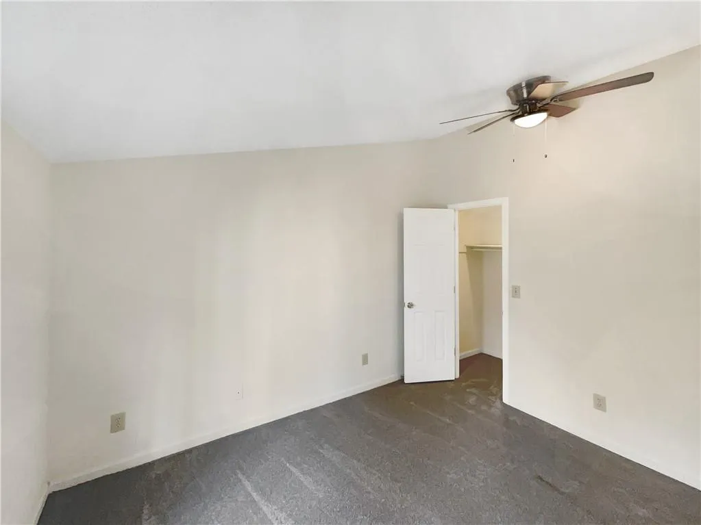 Unfurnished bedroom with a spacious closet, ceiling fan, dark colored carpet, and vaulted ceiling