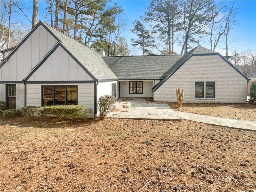 View of front of house with board and batten siding, a patio, brick siding, and roof with shingles