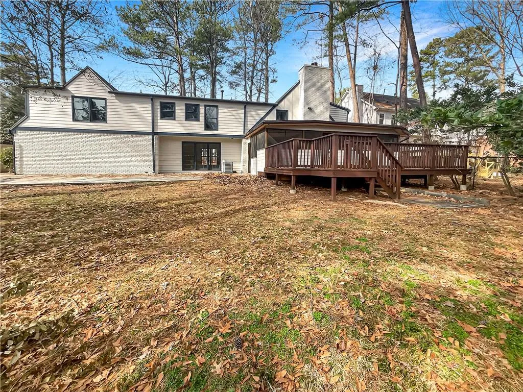 Back of house featuring a deck, brick siding, a chimney, and a lawn