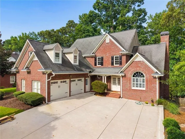 Brick exterior featuring a two-car garage with decorative doors, a broad concrete driveway, and a covered entry porch