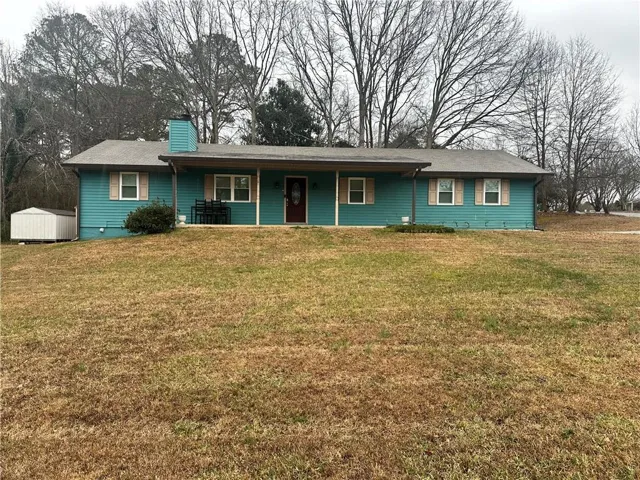 Single-story residence featuring a covered front porch, teal siding, a shingled roof, and a visible storage shed