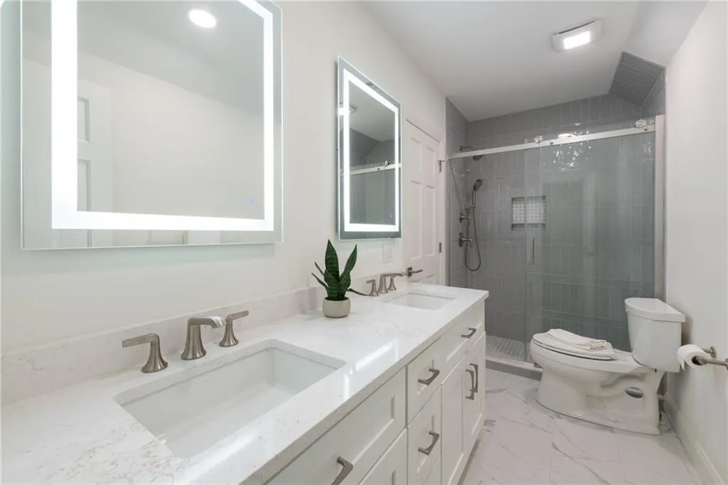 This upper-level bedroom ensuite features dual sinks with quartz countertops and Kohler faucets, a frameless glass shower with Kohler fixtures, dual anti-fog mirrors, and elegant tile in the shower and floor to create a private retreat.