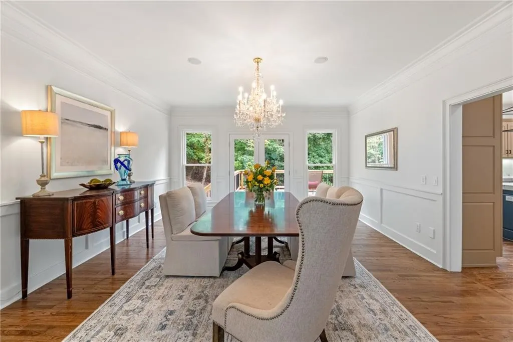 Elegant formal dining room with crystal chandelier, hardwood floors, and abundant natural light, creating a refined space perfect for entertaining and special gatherings. Kitchen entrance to the right.