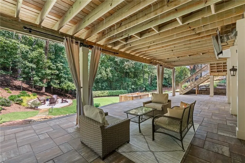 Expansive paver patio with tall ceilings, wired for ceiling fan and TV, outdoor curtains, and serene views of a manicured backyard with private fire-pit.
