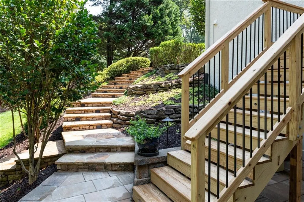 Beautifully crafted stone steps with integrated path lighting leads you to the steps to the upper deck, a level paver patio below deck and a private and manicured backyard.