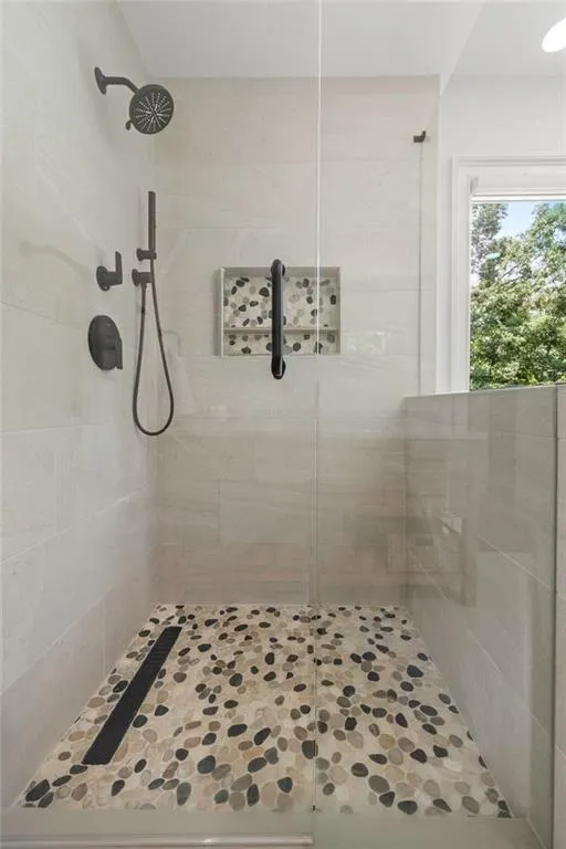 The primary bath features a frameless glass shower with sleek porcelain tile walls, a pebble stone floor, and modern Grohe fixtures, blending spa-like luxury with timeless design.