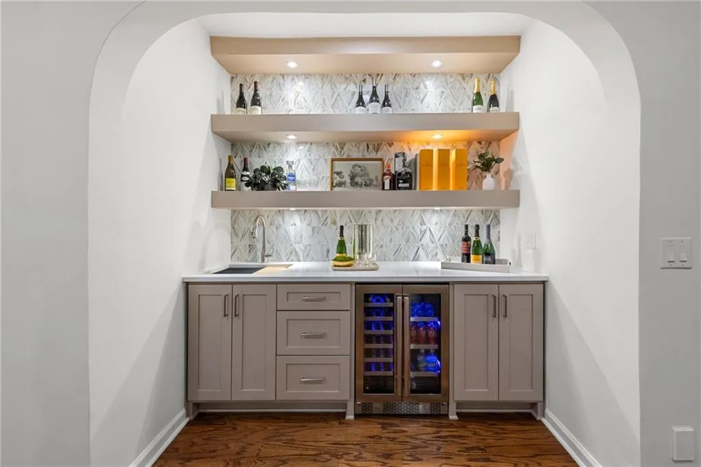 Basement two-tier bar with custom cabinets, quartz countertops, and striking Calico glass backsplash. Features a dual-temperature wine chiller, deep prep sink, cutting board, and mood lighting controls for a stylish, functional entertaining space.