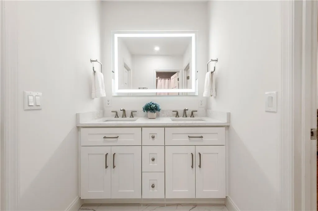 This bath vanity features dual sinks with elegant Kohler widespread faucets, quartz counters, and an anti-fog LED mirror. A separate enclosed space houses the tub/shower combination with cast iron tub and water closet for added privacy and convenience. Flooring in the bath area is a gorgeous white and gray tile.
