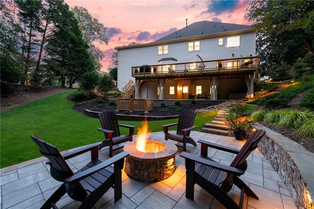 At night, the home transforms with illuminated pathways on both sides leading to the inviting large paver patio with knee wall, where a stone fireplace creates a warm, enchanting ambiance.