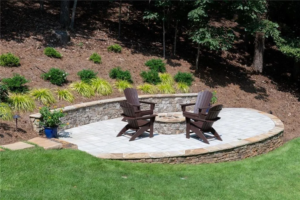 Charming stone paver firepit area with curved retaining wall, lush landscaping, and Adirondack seating, creating a private outdoor retreat perfect for relaxing evenings or gathering with friends under the stars. There's plenty of room to add additional chairs around the fireplace and the patio will easily support an additional sitting area.