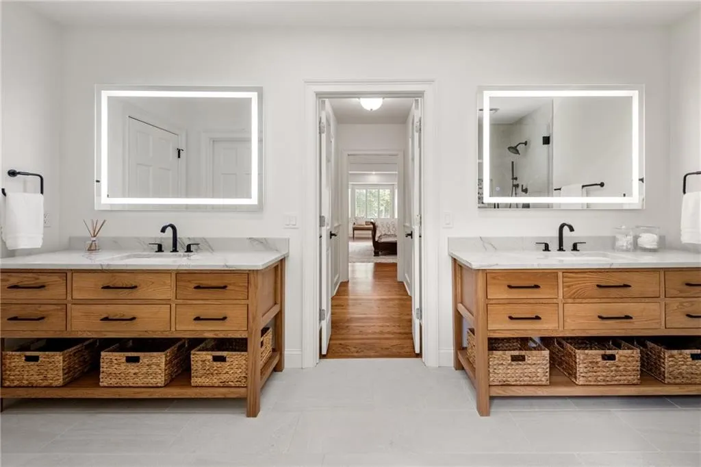 The primary bath showcases dual custom vanities with quartzite countertops, sleek Grohe faucets, and illuminated LED anti-fog mirrors offering adjustable lighting temperatures for a spa-like experience.