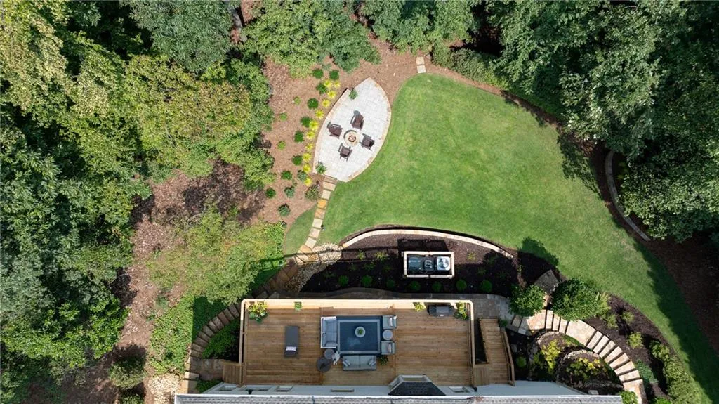 Stunning aerial view highlights the homes' expansive deck, covered patio, and beautifully landscaped private backyard with lush greenery, open lawn, and a stone fire-pit retreat perfect for entertaining or quiet outdoor living.