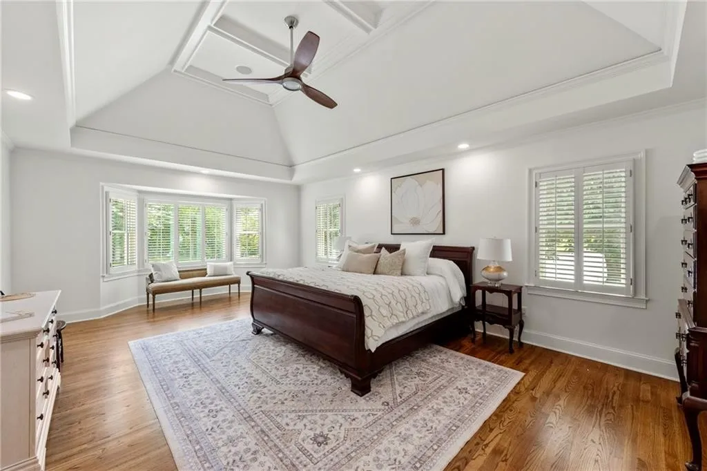 This primary bedroom is a true retreat, showcasing soaring vaulted ceilings, rich hardwood floors, and a serene bay window alcove that floods the space with natural light. The expansive layout easily accommodates a king-sized bed along with multiple pieces of furniture, while recessed lighting and a modern ceiling fan add both comfort and style. Bright and airy, this room balances elegance and relaxation perfect for creating a restful sanctuary.